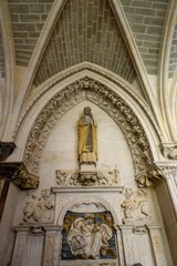 Saint Matthew statue above Renaissance tomb with angelic relief, in Burgos Cathedral.