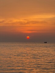 A fiery sun dips gently into the horizon, painting the sky in warm amber and gold. The sea mirrors...