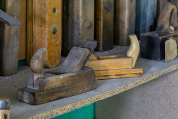 Vintage wooden hand planes displayed on a shelf in a workshop. Various shapes and sizes, traditional woodworking tools.