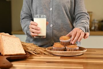 A person is holding a glass of milk and a plate of muffins. The muffins are arranged in a basket on...