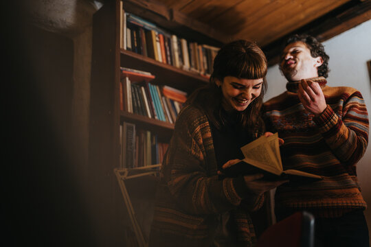 Two friends laughing and reading books while enjoying coffee in a warm library atmosphere.