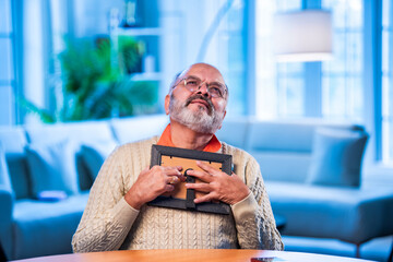 Elderly Indian man holding framed photo with love, lost in memory and emotion