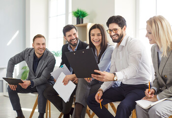 Group of cheerful business people sitting in office, laughing and discussing work documents...