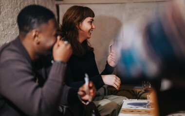 Two friends enjoy a relaxing indoor evening together, laughing and playing cards with warm and cheerful interactions, showcasing their shared happiness and connection during their intimate gathering.