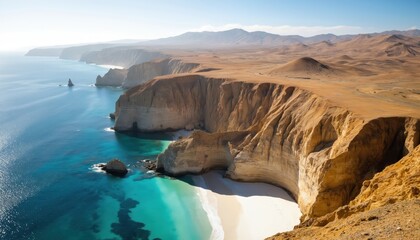 Aerial view of tan sandstone cliffs meeting turquoise ocean waters. Desert hills border white sand beach. Clear sky above rugged coastline and eroded rock formations. Serene natural landscape.