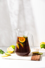 Glass cups and a jug of lemon and lime iced tea on a white table. Sunny day and sharp shadows from glass of lemonade