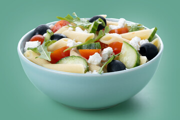 Mediterranean Pasta Salad in bowl with Fresh Vegetables and Herbs on green background