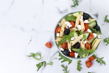 Mediterranean Pasta Salad in bowl with Fresh Vegetables and Herbs on white marble background. Top view. Copy space