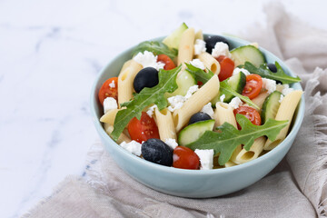 Mediterranean Pasta Salad in bowl with Fresh Vegetables and Herbs on white marble background. Copy space