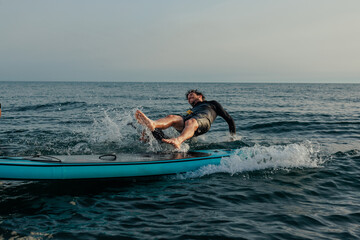 Man falling off a blue paddleboard at sea