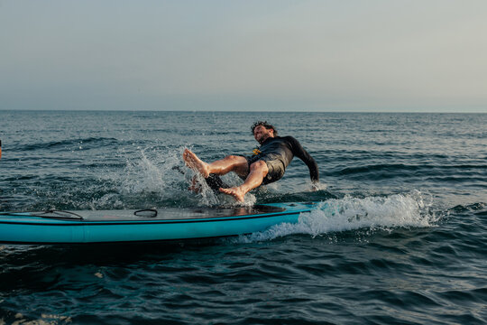 Man falling off a blue paddleboard at sea - Powered by Adobe