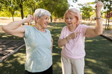 Fototapeta premium Two senior women showing their biceps in a park