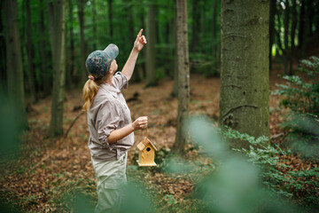 Woman ornithologist pointing toward spot for birdhouse installation in forest habitat, promoting bird nesting and protection
