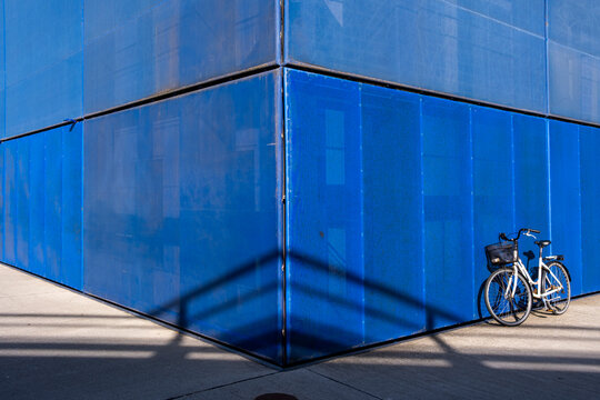 Single bike parked against vibrant blue wall with shadow play in Copenhagen, Denmark, creating contrast and illustrating sustainable choices in modern urban architectural space