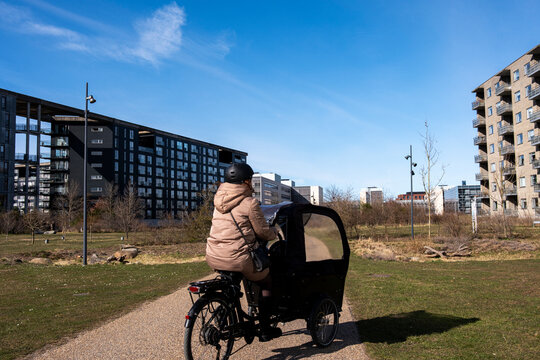 Urban cyclist riding a cargo bike on a sunny day in Copenhagen, showcasing sustainable transportation and slow mobility in a residential green urban planning neighborhood in Denmark