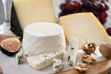 Board of different cheeses with nuts, figs, grapes and wine on wooden table