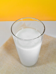 A glass of fresh white cow or goat milk in a glass, isolated on a yellow background and close up shot.