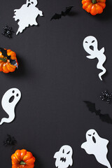 Halloween flat lay with paper ghosts, bats, spiders, and pumpkins on black. Frame of spooky...