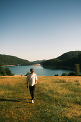 A man is walking through a serene field, with a lake behind