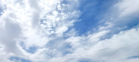 Fototapeta premium A clear, bright blue sky filled with scattered, fluffy white cumulus clouds on a sunny day.