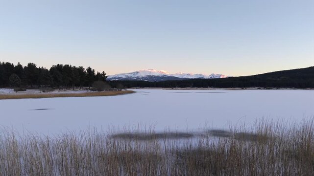 Amazing drone movement over Laguna La Zeta frozen lake with reeds and beauty of snowy distant mountain peaks, Esquel, Province of Chubut, Argentina.