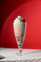 Milkshake with berry topping and foam on red background