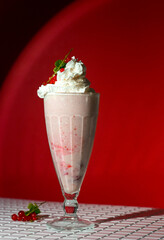 Milkshake with berry topping and foam on red background