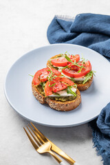 Healthy sesame toast with tomatoes, mozzarella, arugula and pesto on a blue plate on light background