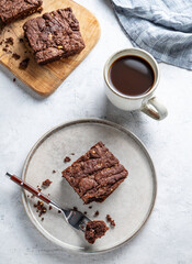 Chocolate brownie on a plate on a light background with cup of freshly brewed coffee and napkin.
