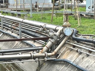 Industrial piping system with large metal valves and multiple pipelines installed along drainage,...