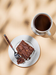 Chocolate brownie on a plate on a beige background with cup of freshly brewed coffee