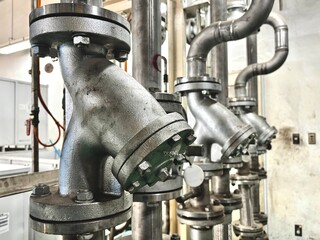 Industrial Y-strainer valve on steel piping system with flange connection in outdoor chemical plant. High-resolution close-up detail of metal filter for mechanical fluid filtration.