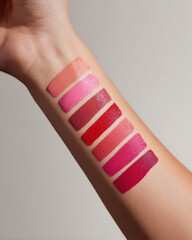 Close up view of female forearm displaying swatches of various matte lip colors, showcasing gradient from soft nude to vibrant pink and deep red shades. image captures beauty and diversity of lip