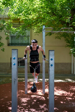 Determined male athlete performing weighted dips on parallel bars in outdoor calisthenics park