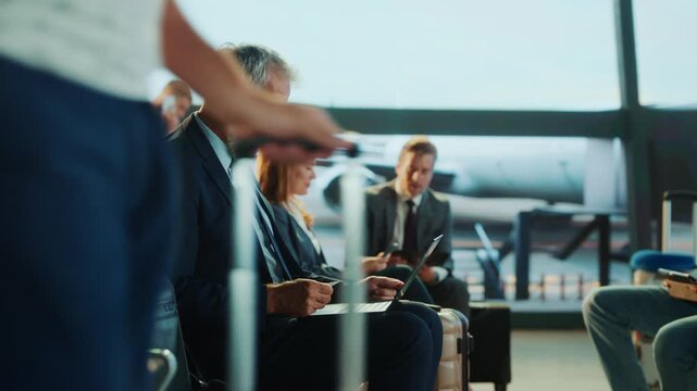 A businessman in a suit is engrossed with his phone while waiting at the airport. Other passengers are also present.