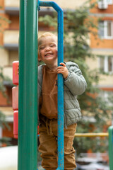Obraz premium Vertical portrait of a small red-haired boy who looks over the fence of a playground in the city. Outdoor games