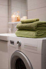 Green folded towels stacked on white washing machine in bright modern bathroom interior with soft lighting