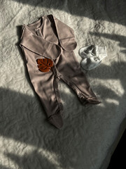 A dark beige suit for a newborn is lying in the sun on a white bedspread. Preparation for discharge from the hospital. Waiting for a miracle