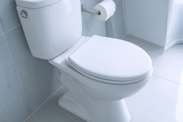 clean white toilet with closed lid in modern bathroom featuring tiled walls and floor, toilet paper holder on the wall