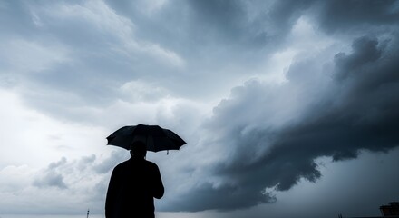 Silhouette of Person Holding Black Umbrella Against Dramatic Storm Clouds