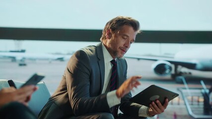 A businessman in a suit is seated in an airport terminal, using a tablet while waiting for his flight. - Powered by Adobe