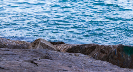 Rocks along the shoreline meet the calm blue waters of the sea, showcasing the tranquil beauty of nature and the peaceful essence of a coastal landscape.