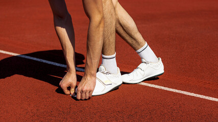 Athlete in starting stance on red track surface under bright sunlight preparing to sprint. Concept of motion start, track surface texture, training beginning, moment of readiness