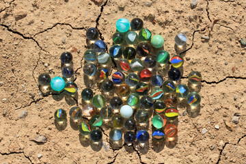 Different colored glass marbles found on brown soil. Marbles are a children's plaything.