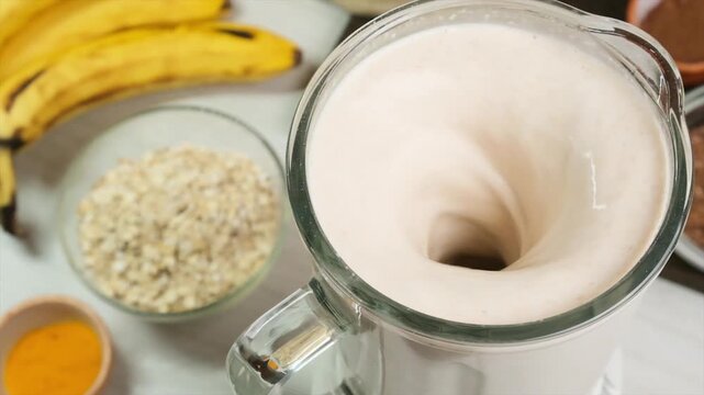 Close-up top view of a blender mixing a smoothie made from fruit, nuts, and oat milk. Slow swirling motion. Fully vegan drink without animal fat. Healthy plant-based cocktail after workout.