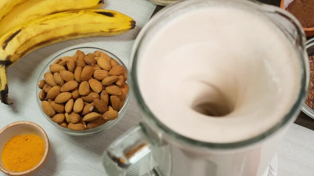 Top view of slow blending vegan smoothie with nuts, seeds, turmeric, cocoa, pepper, and almond milk. Raw plant-based drink without heat or animal fat. Clean eating and vegan nutrition.