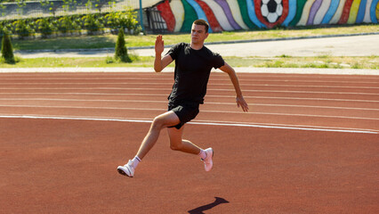 Young runner dashing on track with mural backdrop. Concept of running phase in pole vault, speed...