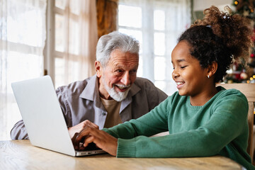 Mature couple with grandchild look at laptop screen and learn how to make video call or use laptop