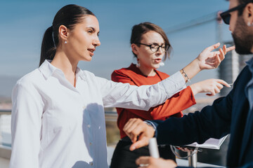 A group of business colleagues engaged in discussion on a rooftop. They are pointing and gesturing...