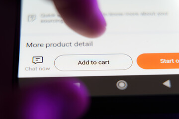 Close up of white Add to cart button on smartphone screen with user's fingers above.